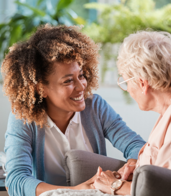 Caregiver smiling and holding hands with an older woman during a first home visit.