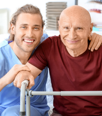 Smiling male EverCare caregiver standing beside an older man using a walker at home.