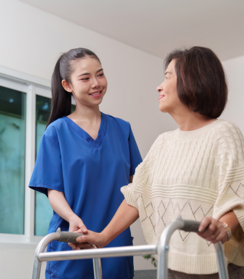 Caregiver in blue scrubs smiling with an older woman using a walker — companion-tier home support.