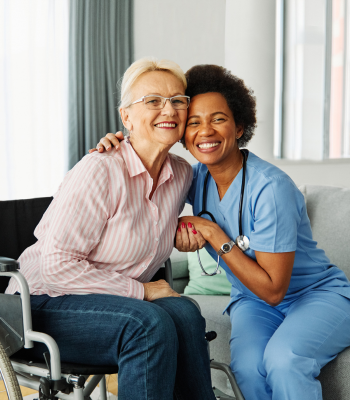 Smiling caregiver beside an older woman in a wheelchair — 24-hour memory care companionship at home.